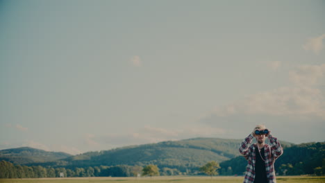 Male-Tourist-Looking-Through-Binocular-Standing-In-Meadow