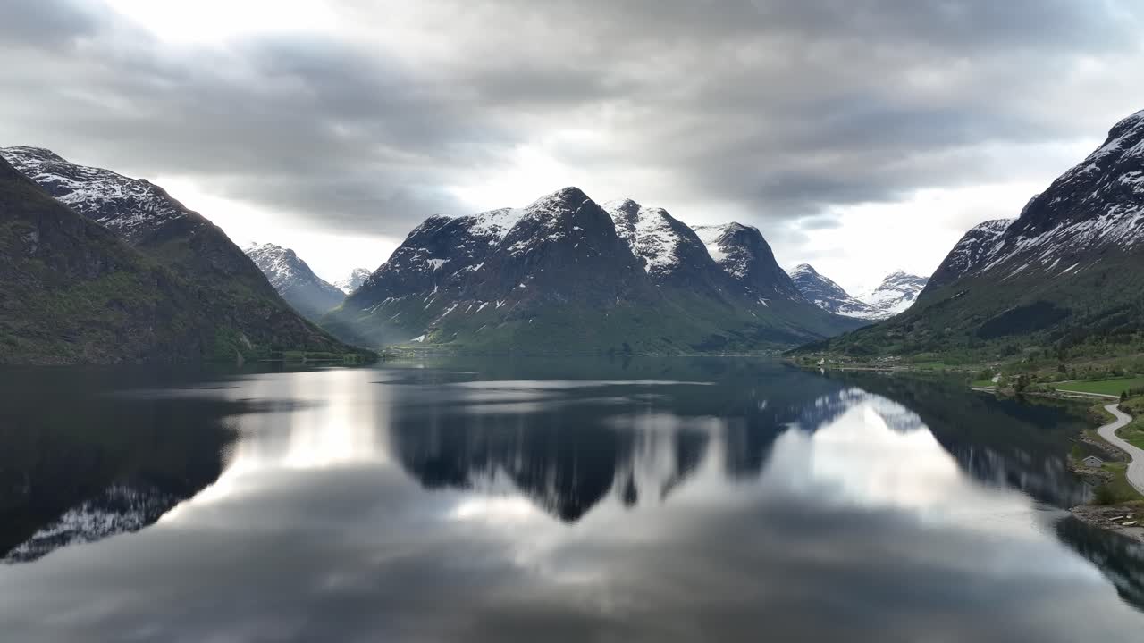 levantamiento de la mañana aérea por encima del lago oppstrynsvatnet con impresionante paisaje de montaña de fondo y surays penetrando a través del valle a la izquierda - mounain reflejos en la superficie del agua