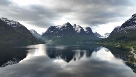 Aufsteigende-Morgenantenne-über-Dem-See-Oppstrynsvatnet-Mit-Atemberaubender-Berglandschaft-Im-Hintergrund-Und-Durch-Das-Tal-Eindringenden-Surays-Auf-Der-Linken-Seite---Bergspiegelungen-In-Der-Wasseroberfläche