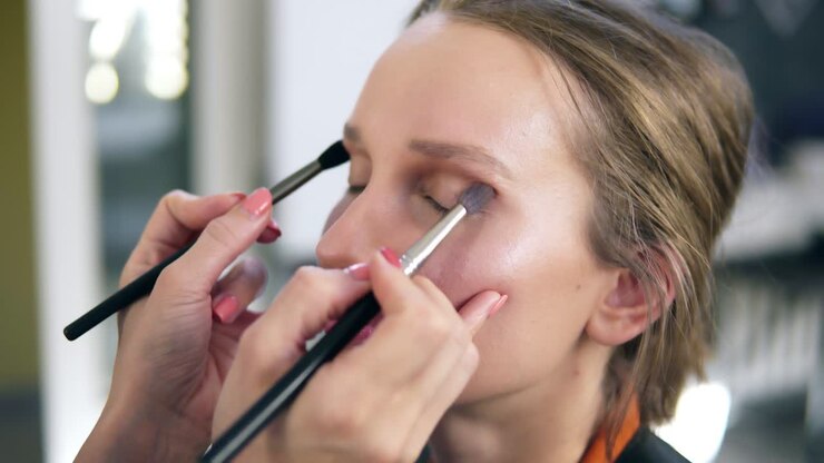 The professional make-up artist does make-up for the young cute model. Artist putting and eyes shadows using two brushes and does