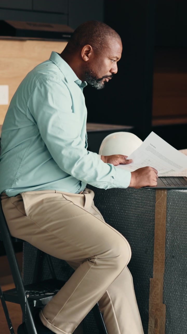 Architect Reviewing Blueprints and Working on Laptop at Construction Site