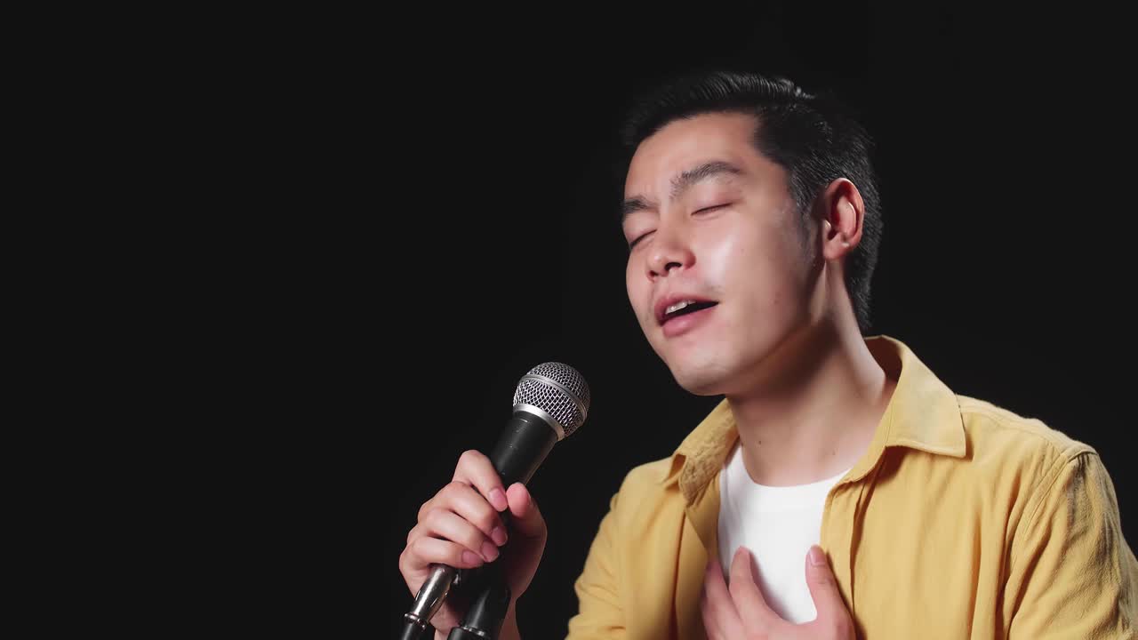 Side View Of Asian Man Singer Singing Into Microphone On Black Background