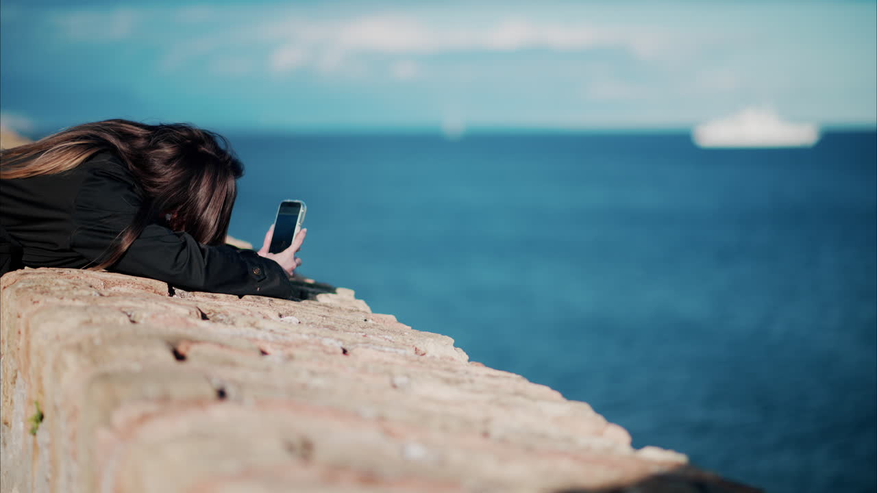 Young woman taking pictures of the sea with her phone in Antibes, France