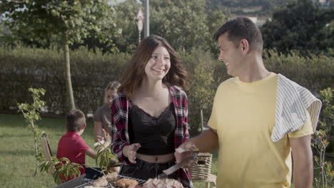 happy teenage daughter talking to father while he cooking meat