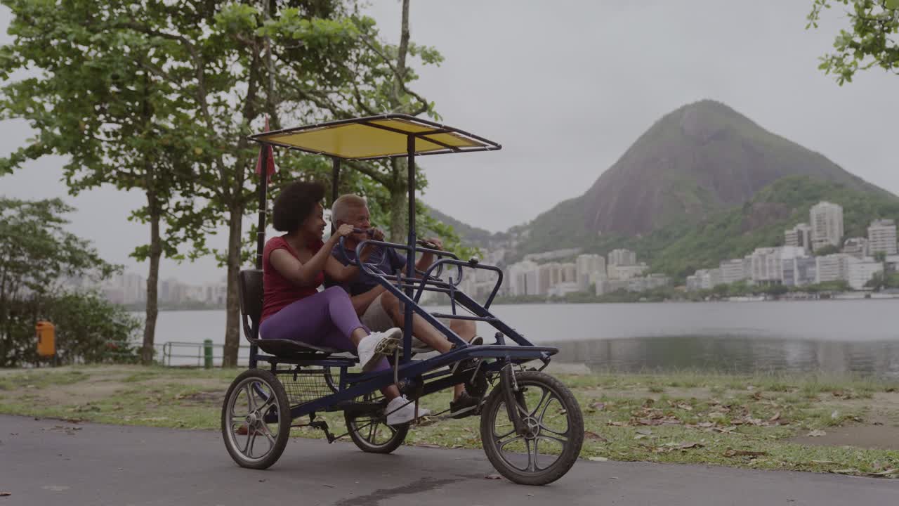 Couple Riding a Pedal Bike by the Lake with a Mountain and City View