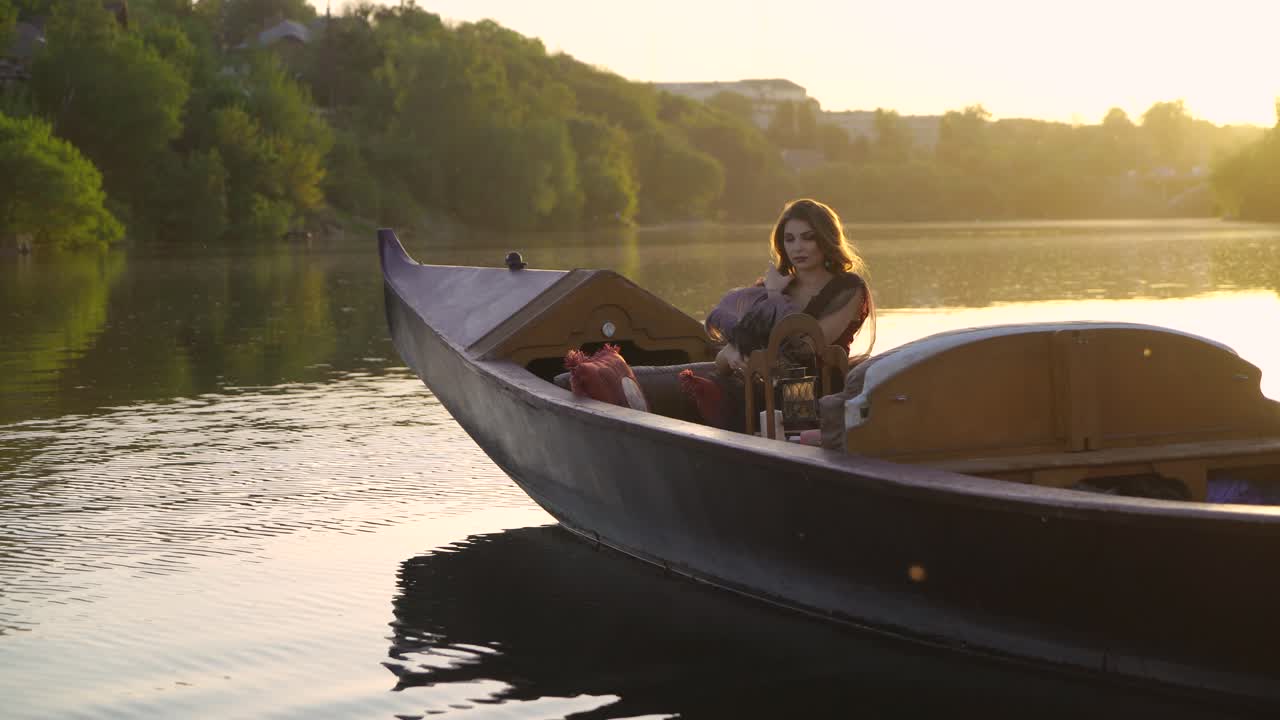 A beautiful woman with long hair is sitting in a gondola in an elegant dress at sunset. Carnival in Venice