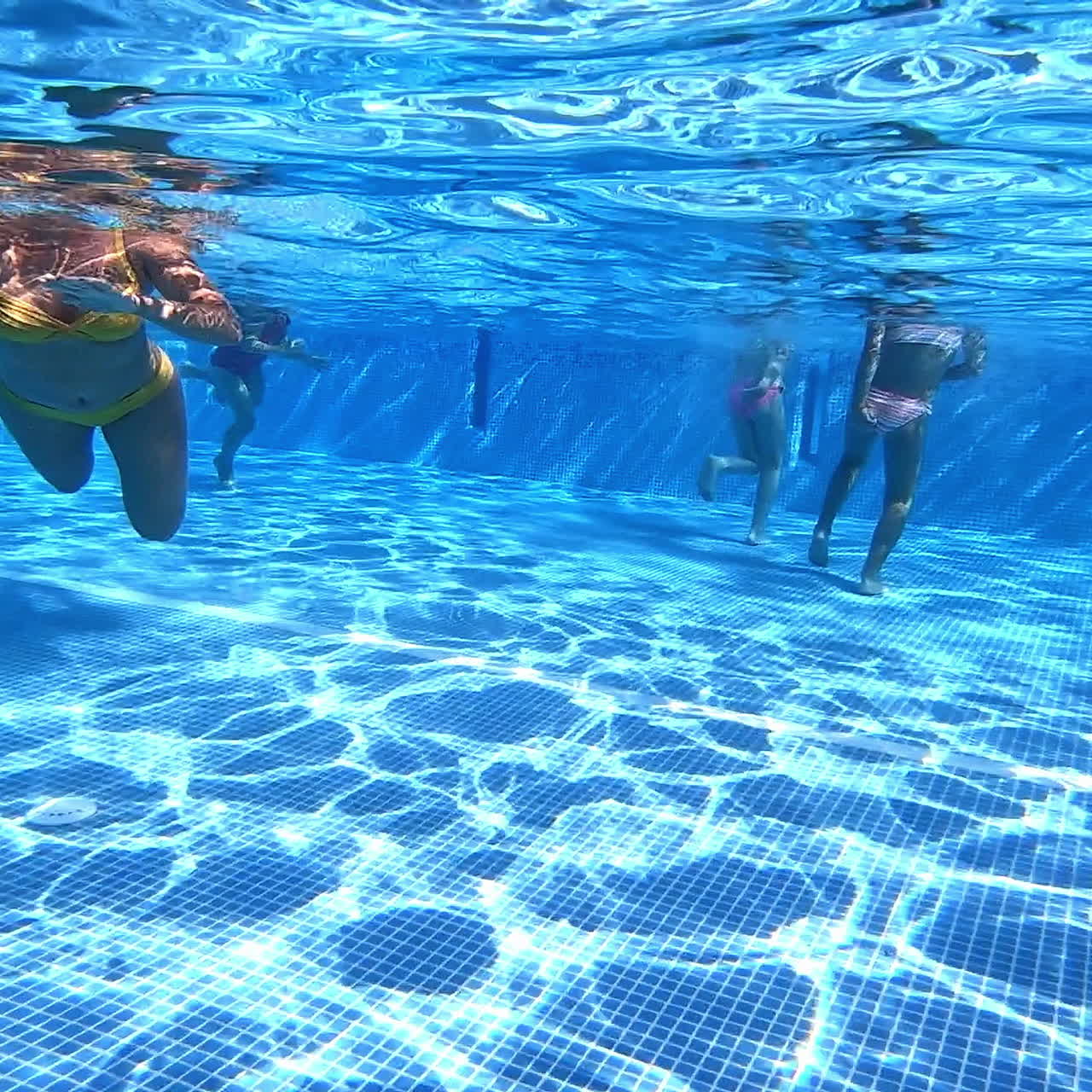 People swimming in the swimming pool. Underwater video of children's legs and woman's body swimming in transparent blue water.