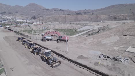 un avión no tripulado gira sobre maquinaria de construcción pesada estacionada fuera de un sitio de construcción de la casa, listo y listo para comenzar el trabajo