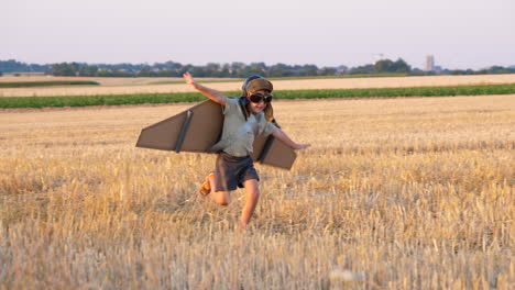 little boy with cardboard wings vintage pilot helmet plays in field