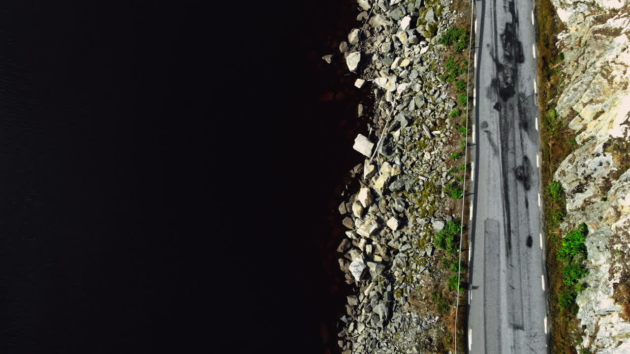 vista aérea sobre una carretera en la costa de un lago, día soleado, en suecia - de arriba hacia abajo, disparo de drones