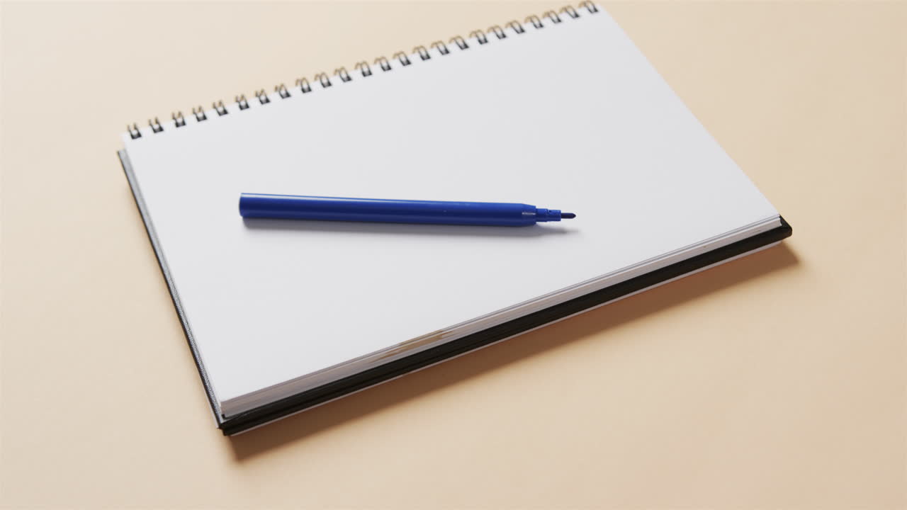 Close up of blue marker on notebook with beige background, in slow motion