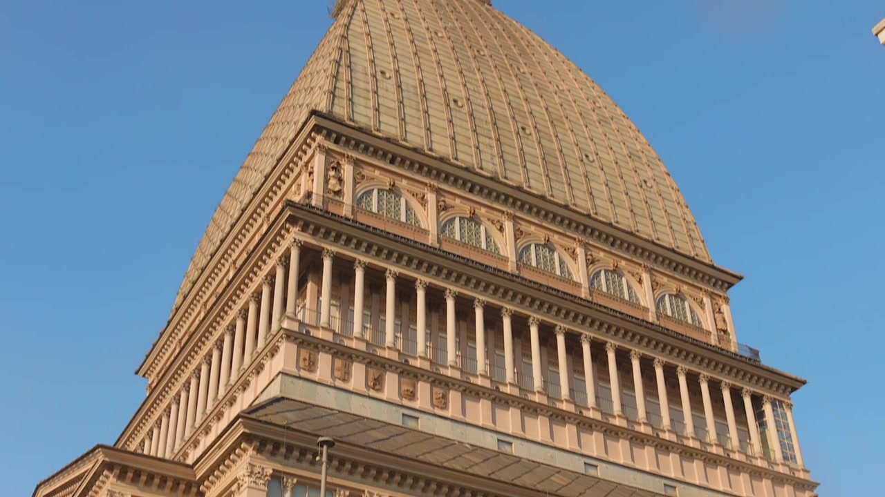 Panoramica verso l'alto dell'esterno della Mole Antonelliana a Torino, che mostra l'architettura dettagliata alla luce del sole.