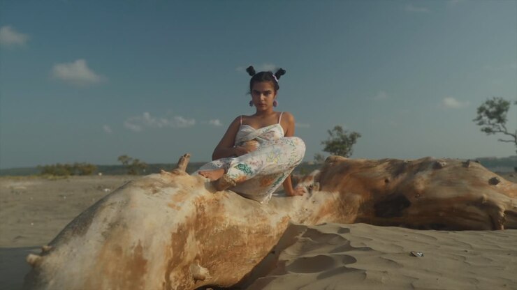 A beautiful Indian model poses for a brand shoot sitting on a large beam, by the sea