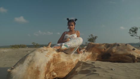 a beautiful indian model poses for a brand shoot sitting on a large beam, by the sea