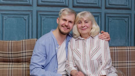 семья старшей матери и красивого взрослого сына или внука смотрят в камеру, домашние выходные