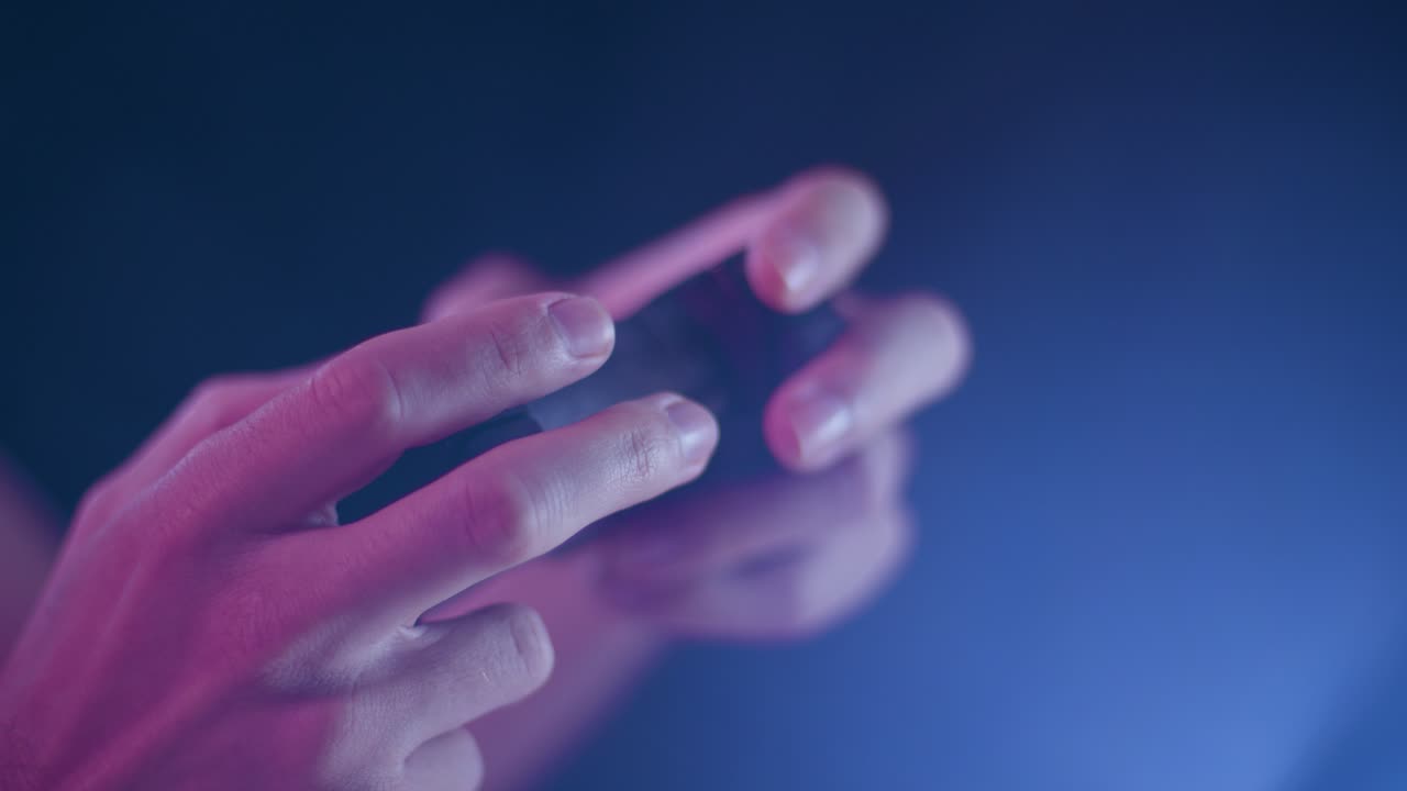 Playing video games on a small controller using triggers playing slowly with blue lens flare black background