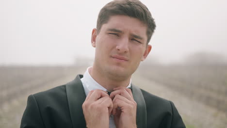 man in tuxedo adjusting bow tie in a field