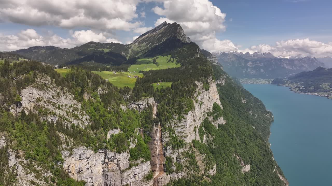 Breathtaking aerial shot of a high alpine cliff with cascading waterfall above Walensee in Switzerland, showcasing dramatic mountain scenery, lush forests, and turquoise lake waters