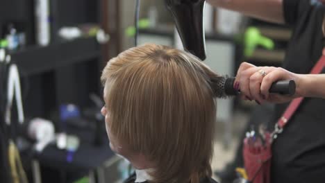 peluquero profesional usando un secador de pelo después del corte de pelo. mujer joven vistiendo su cabello en una peluquería. estilista