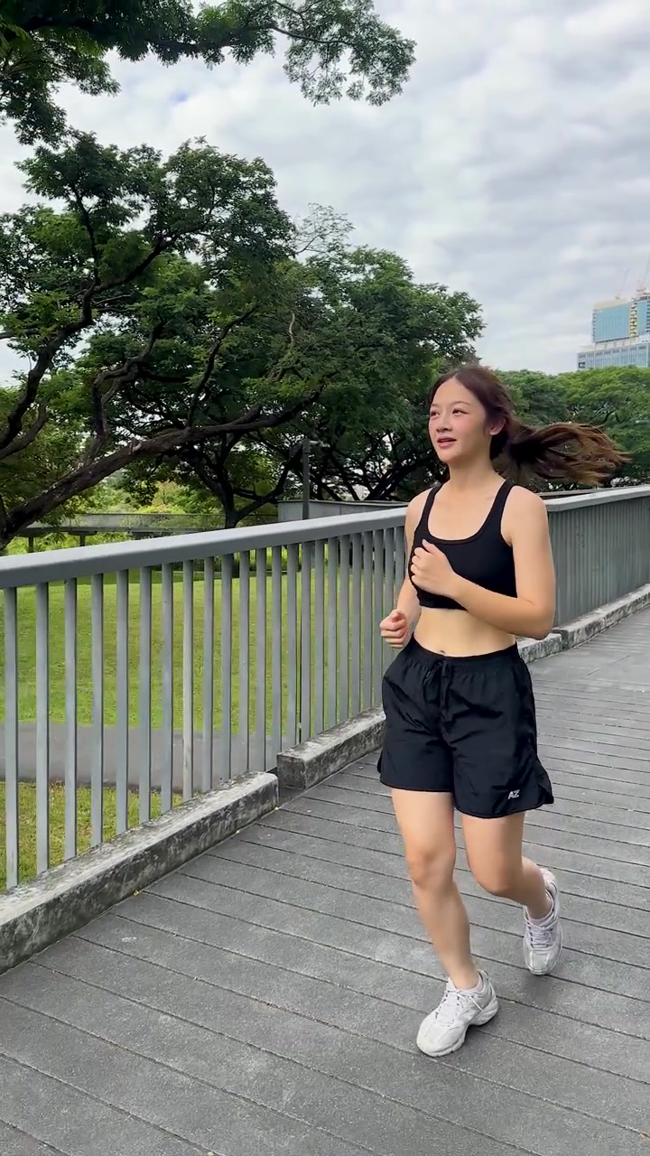Una giovane donna in abbigliamento sportivo nero fa jogging su un ponte del parco sotto la luce diurna nuvolosa