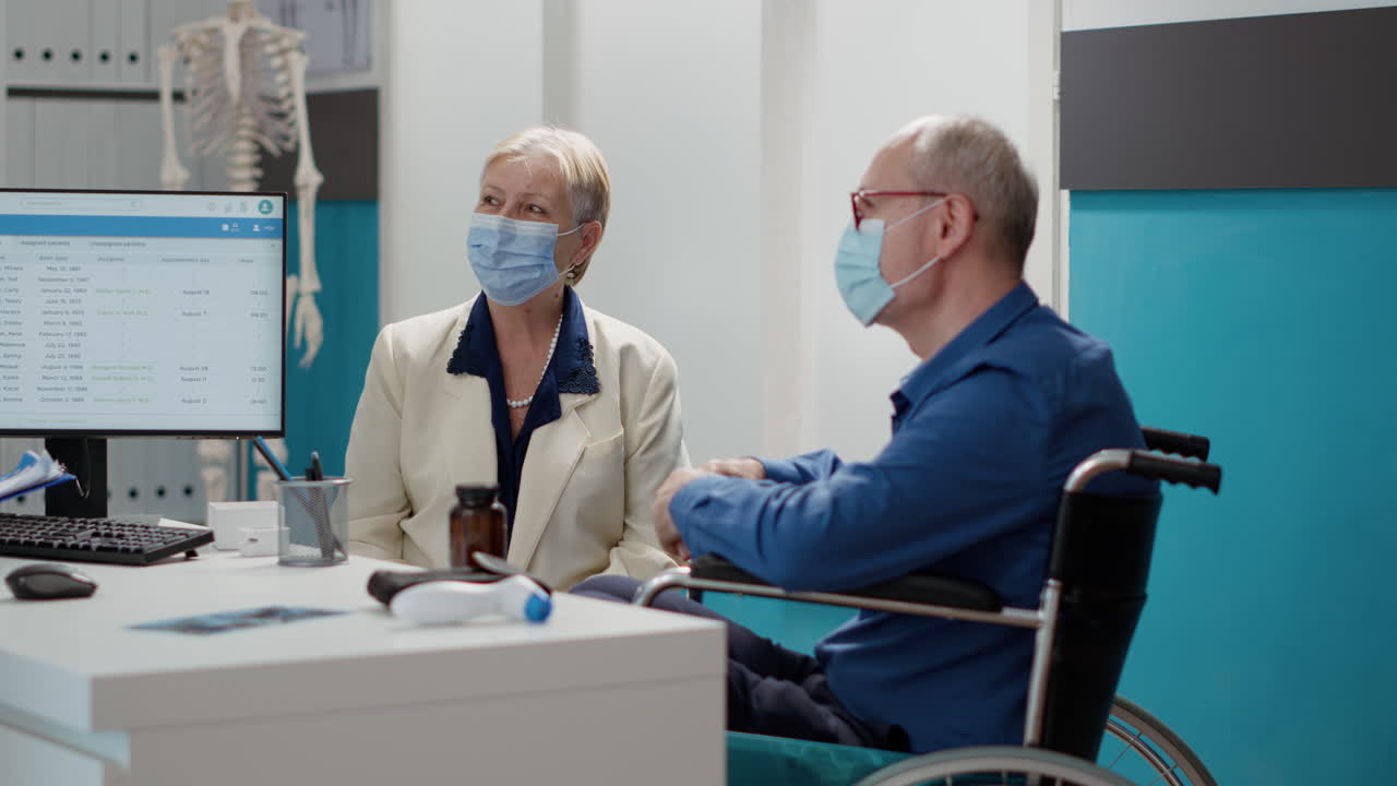 Doctor Consulting with Elderly Patient in Wheelchair Wearing a Face Mask