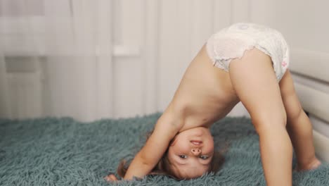 una linda niña de dos años está haciendo el ejercicio del puente mientras usa un pañal