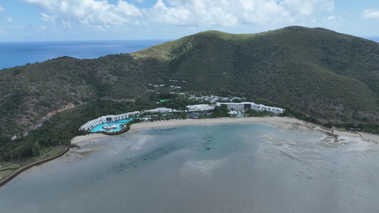 Cảnh quay drone chậm từ từ tiến vào ban ngày, đến gần khu nghỉ dưỡng Hayman Island, bãi biển và vịnh đầm phá nông tại Whitsundays, Queensland, Úc