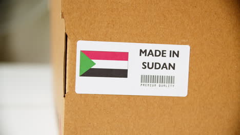 hands applying made in sudan flag label on a shipping cardboard box with products. close up shot with premium quality barcode.