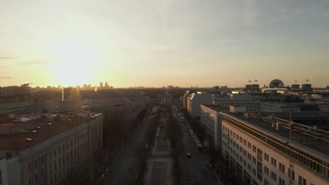 AERIAL:-Scenic-low-flight-through-busy-Berlin,-Germany-Street-towards-Brandenburg-Gate-in-beautiful-golden-sunset-light