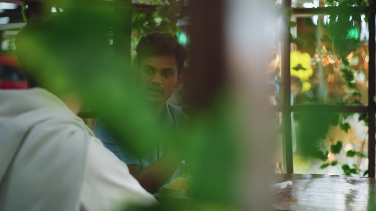 Round view showing colleagues discussing while artificial flowers hang from pillars, soft ambient light reflecting on surfaces, focus on interaction and decorative installation in communal space