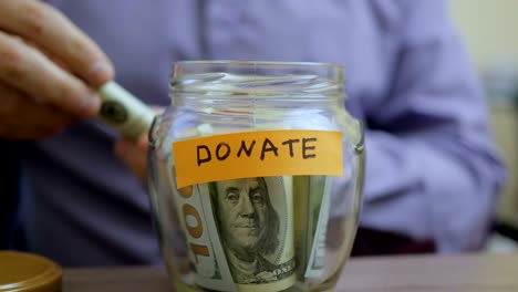 hombre caucásico poniendo un frasco de vidrio puesto en una mesa de cajón con sus ahorros para donar