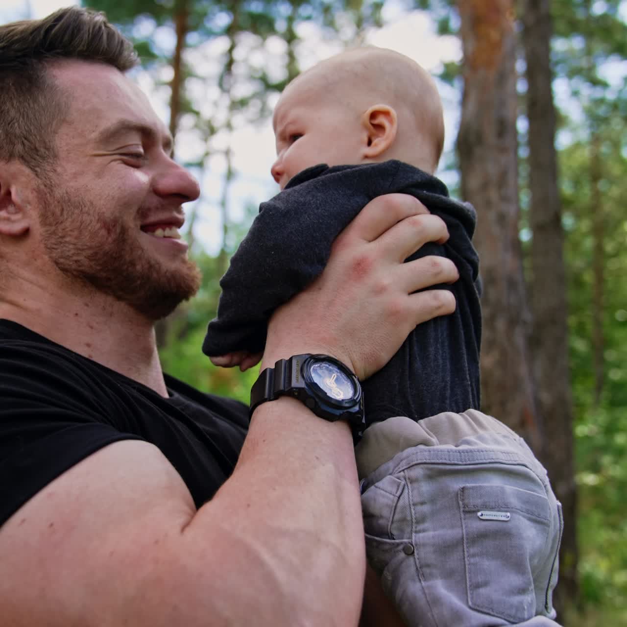 Uomo caucasico felice che tiene un neonato davanti alla sua faccia. Papà affettuoso che bacia il suo figlioletto. Sfondo naturale. Video verticale