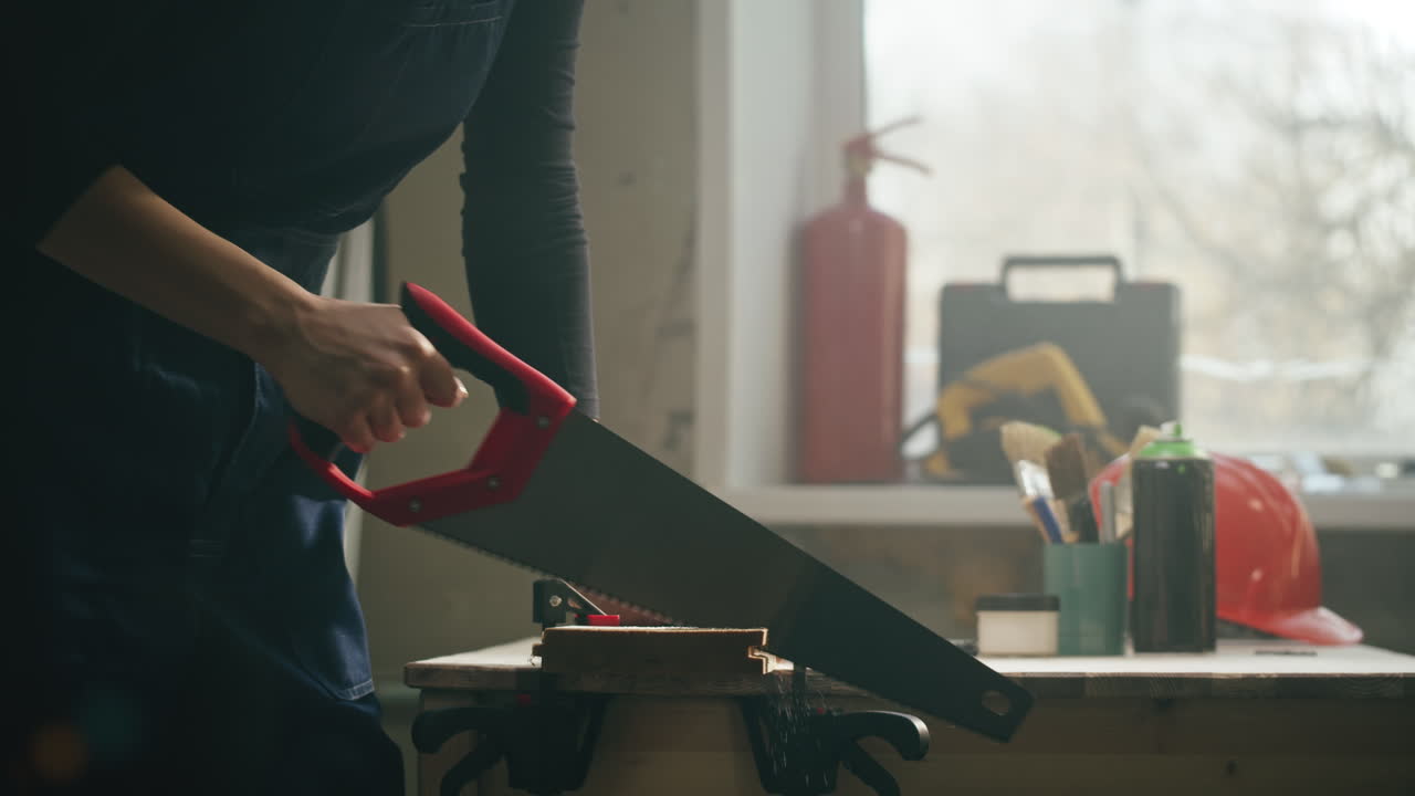 Person Sawing Wood with a Handsaw in a Workshop