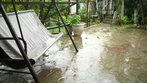 swaying in the wind wet country swing in the country summer house in heavy rain. circles of raindrops and huge puddles on the asphalt.