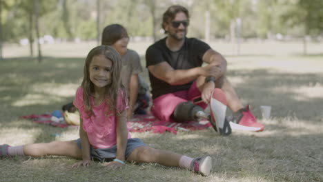 happy girl sitting in leg-split on lawn during picnic