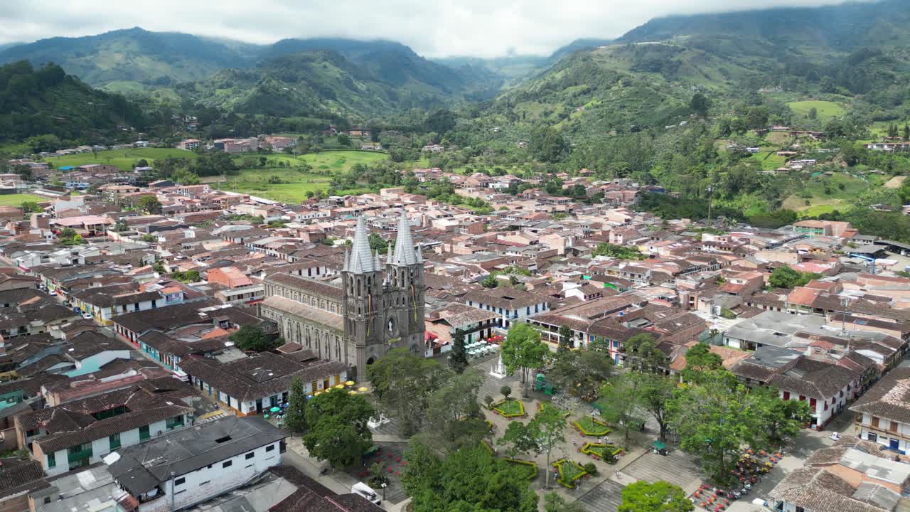 Aerial drone footage of the picturesque Andean town of Jardín in Colombia, featuring the central square, the church Basílica Menor de la Inmaculada Concepción and the surrounding mountain landscape