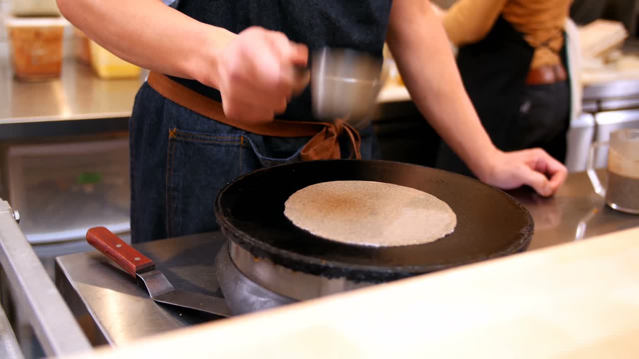 chef vertiendo masa líquida en la sartén caliente mientras prepara crepes