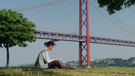 woman reading a book in a park by the bridge