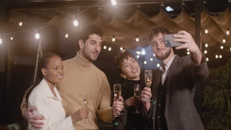 Grupo-De-Cuatro-Felices-Amigos-Multiétnicos-Con-Copas-De-Champán-Tomando-Una-Foto-Selfie-En-La-Fiesta-De-Fin-De-Año