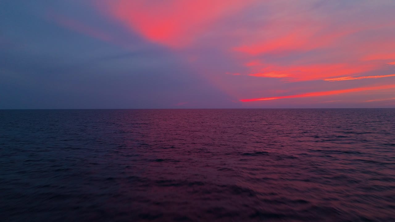 夕暮れの海、穏やかな水面に鮮やかなピンクと紫の色合いが反射し、静寂な景色を作り出す