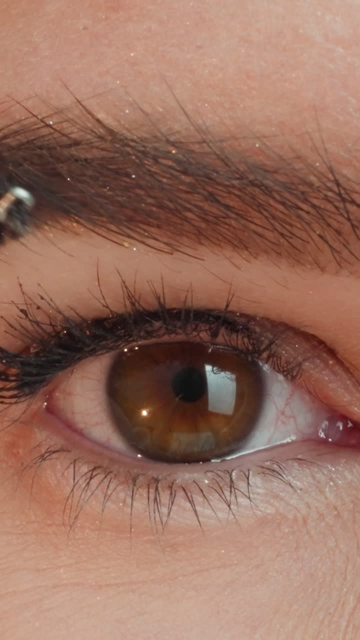 Young woman combs thick eyebrows with brush to make good shape. Stylish lady uses cosmetic product for doing professional makeup extreme closeup