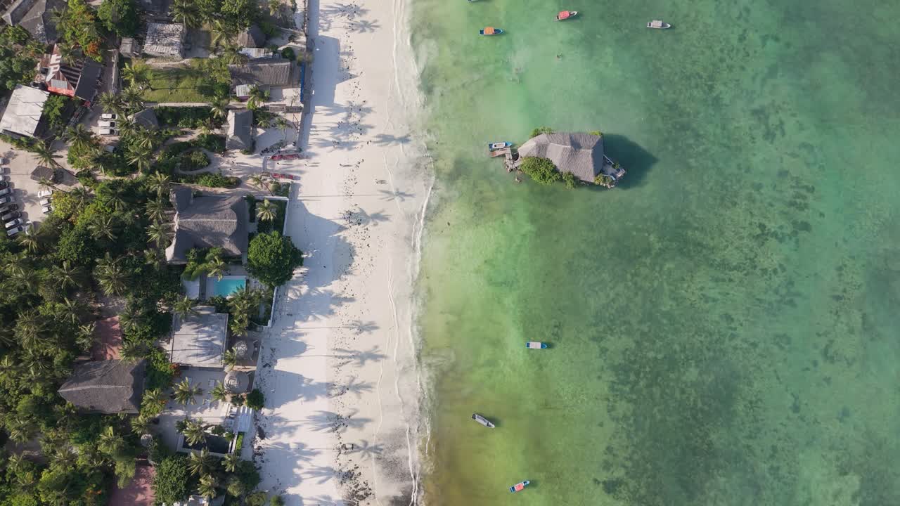 vista aérea mirando hacia abajo sobre el restaurante rock zanzíbar durante la hora dorada con sombras de palmeras en la costa de la estación de arena blanca africana