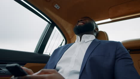African-businessman-looking-smartphone-at-car.-Afro-man-holding-phone-at-vehicle