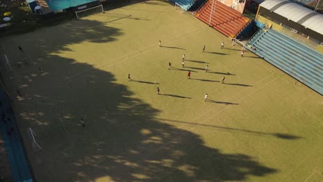 aerial view showing teenager playing football on soccer field during sunset - training session at club of buenos aires