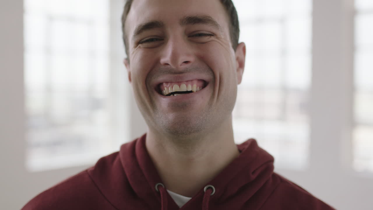 retrato en primer plano de un apuesto joven caucásico riendo ventanas alegres fondo del apartamento