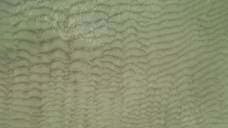 aerial: medium shot of top view shot of waves on the shallow shore and spilling on sand