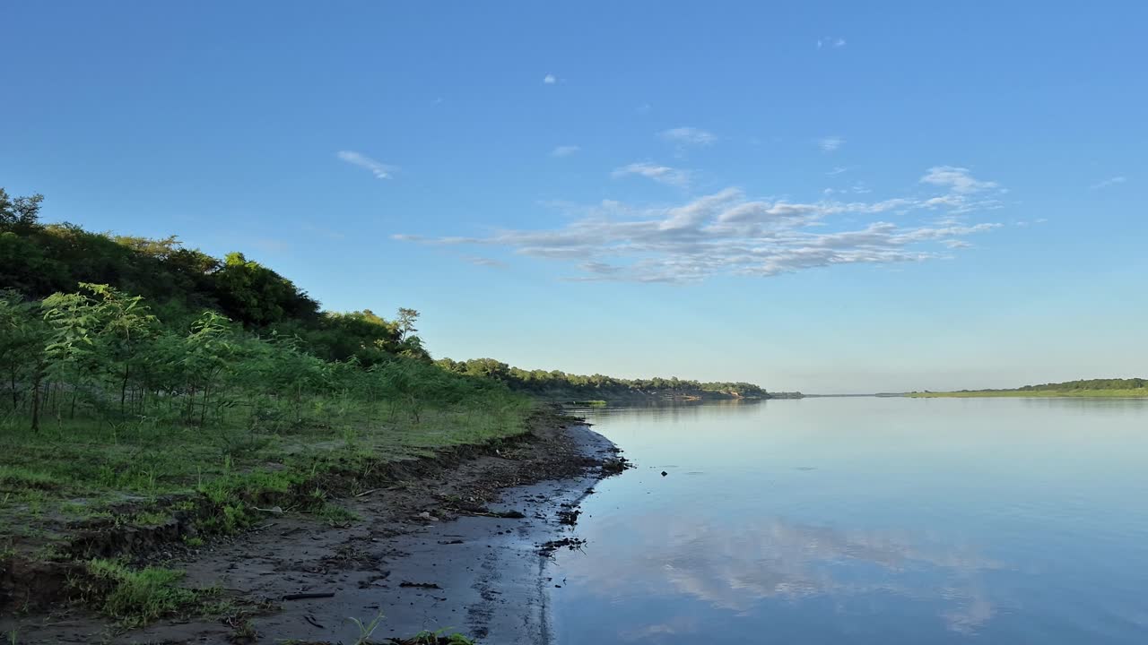 Riverbank reveals the majestic Paraguay River with clouds reflected in the water at sunrise. Shot in 4K at 60fps, ideal for nature videos and tranquil landscapes