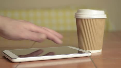 hands holding a takeaway coffee to-go with tablet medium shot