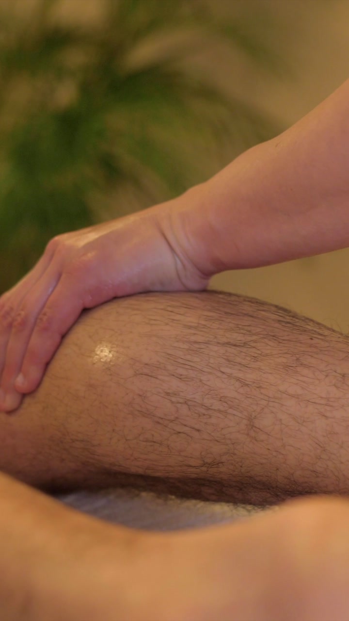 female masseuse massaging male leg slow motion, vertical closeup indoor beauty salon