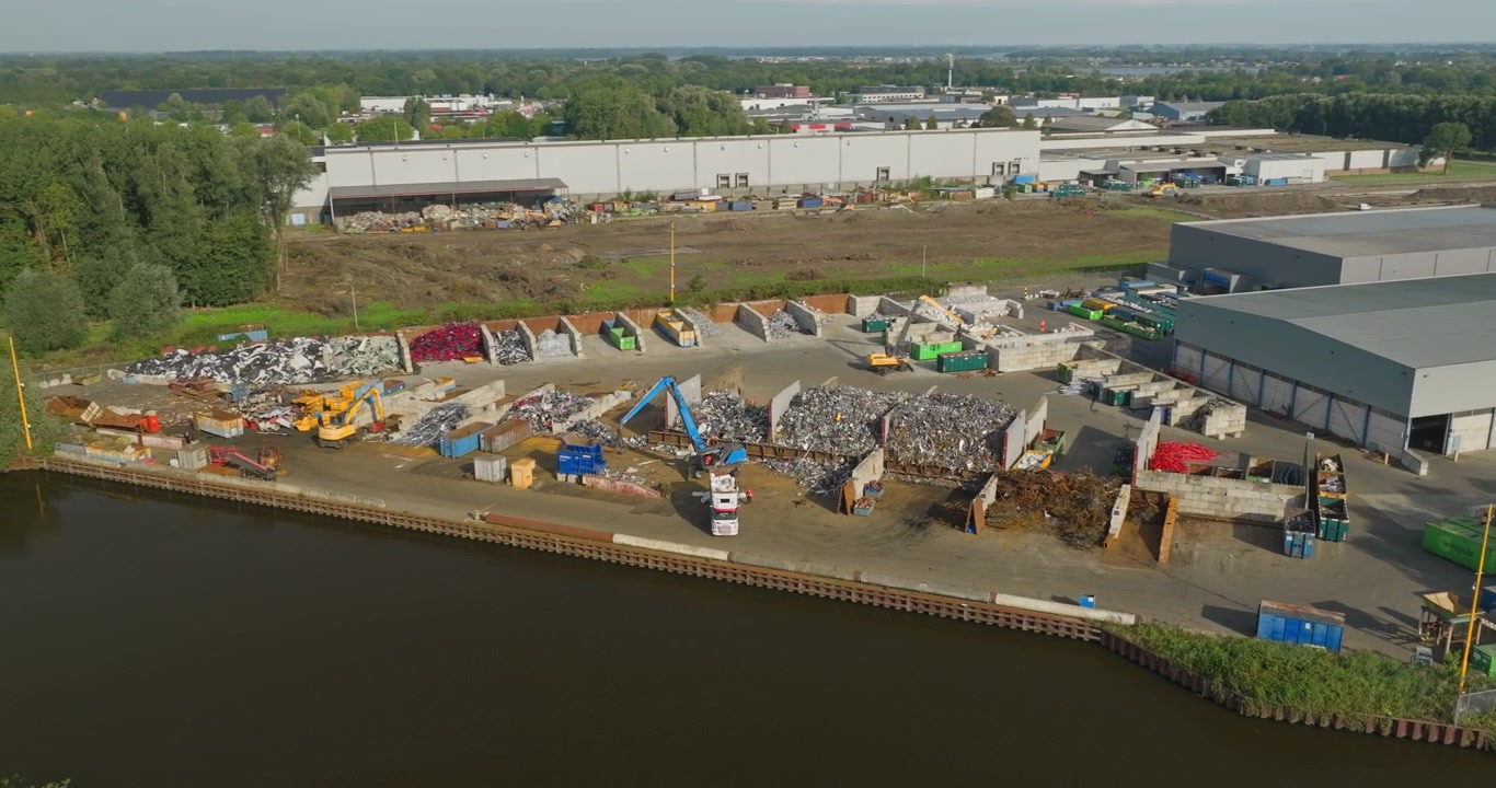 Orbita aerea di drone attorno a un deposito di riciclaggio di rottami metallici che mostra enormi cumuli di metallo scartato, macchinari industriali e contenitori pieni di rifiuti metallici riciclabili